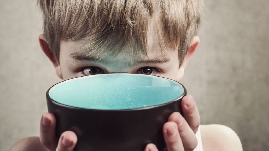 A young hungry boy holding an empty bowl up and close to his face